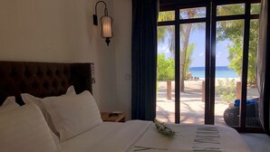 Habitación de hotel con una cama grande, una mesita de noche, una lámpara de pared y vistas a la playa desde la ventana.