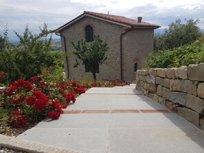Ein Gebäude aus Stein mit einem Ziegeldach, umgeben von einer Steinmauer und einem mit roten Blüten bepflanzten Weg.