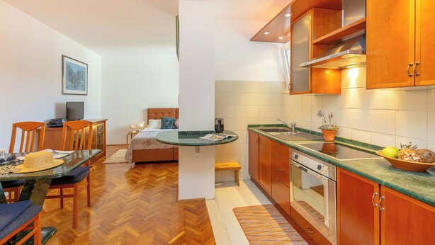 Une cuisine compacte avec des meubles en bois, un four encastré et un coin repas comprenant une table et des chaises en verre.