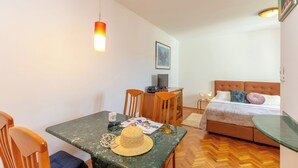 Une pièce comprenant un lit, un bureau avec un ordinateur, une table à manger avec des chaises, et un chapeau posé sur la table.