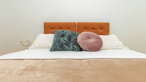 Un lit avec une tête de lit marron, une literie blanche et trois oreillers aux motifs et aux couleurs différents.