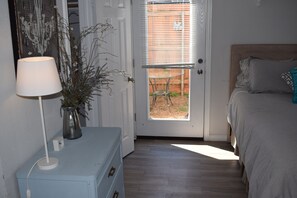 A bedroom with a bed, a dresser, a lamp, and a door leading to an outdoor area. - Neat Suite is a downstairs studio (McKinney)