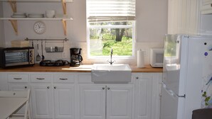 Een keuken met witte kasten, een houten aanrecht, een spoelbak, een magnetron, een koelkast en een raam met uitzicht op groen.
