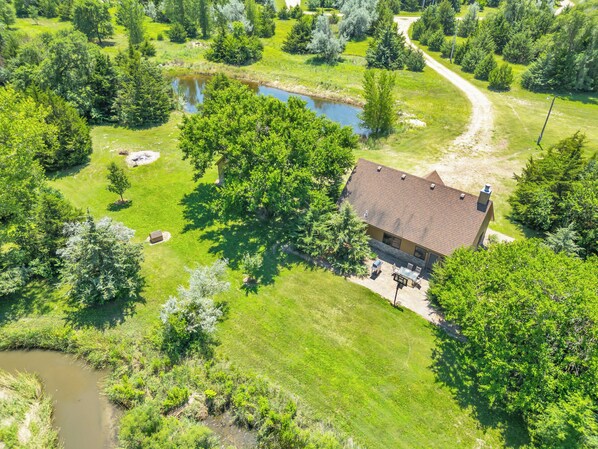 A house with a patio and a pond in a lush green landscape. - Rustic Cottage Retreat (Kearney)