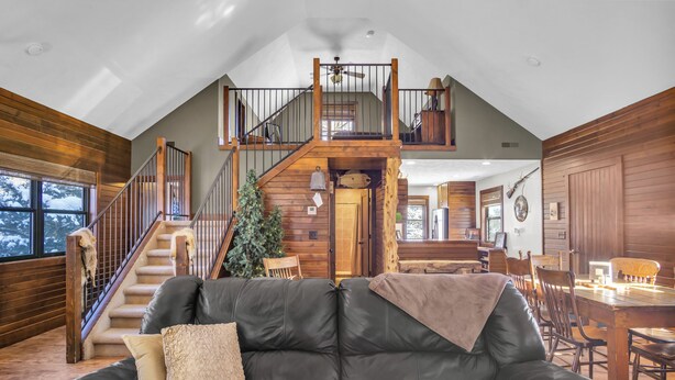 A spacious living area with a leather sofa, wooden staircase, and a dining area with wooden furniture.