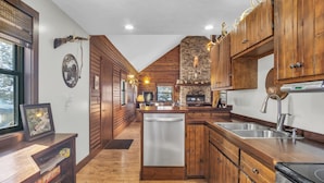 A kitchen with wooden cabinets, a stone fireplace, and a dishwasher.