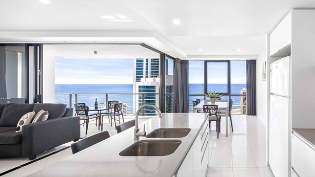 A modern kitchen with a large island, a dining area with chairs and a table, and a view of the ocean. - Circle on Cavill Ocean & River Views (Surfers Paradise)