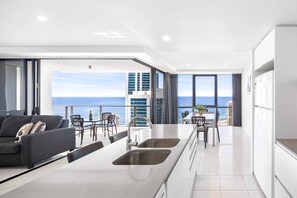 A modern kitchen with a large island, a dining area with chairs and a table, and a view of the ocean. - Circle on Cavill Ocean & River Views (Surfers Paradise)