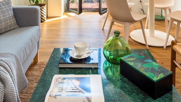 Een moderne woonkamer met een bank, een salontafel, een eettafel met stoelen, een potplant en uitzicht door een glazen deur.