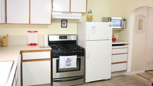 Cucina con mobili bianchi, piano cottura in acciaio inossidabile, frigorifero bianco e forno a microonde.