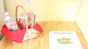 Een mand met waterflesjes, snacks en een handleiding van Star Cottage op een houten vloer.