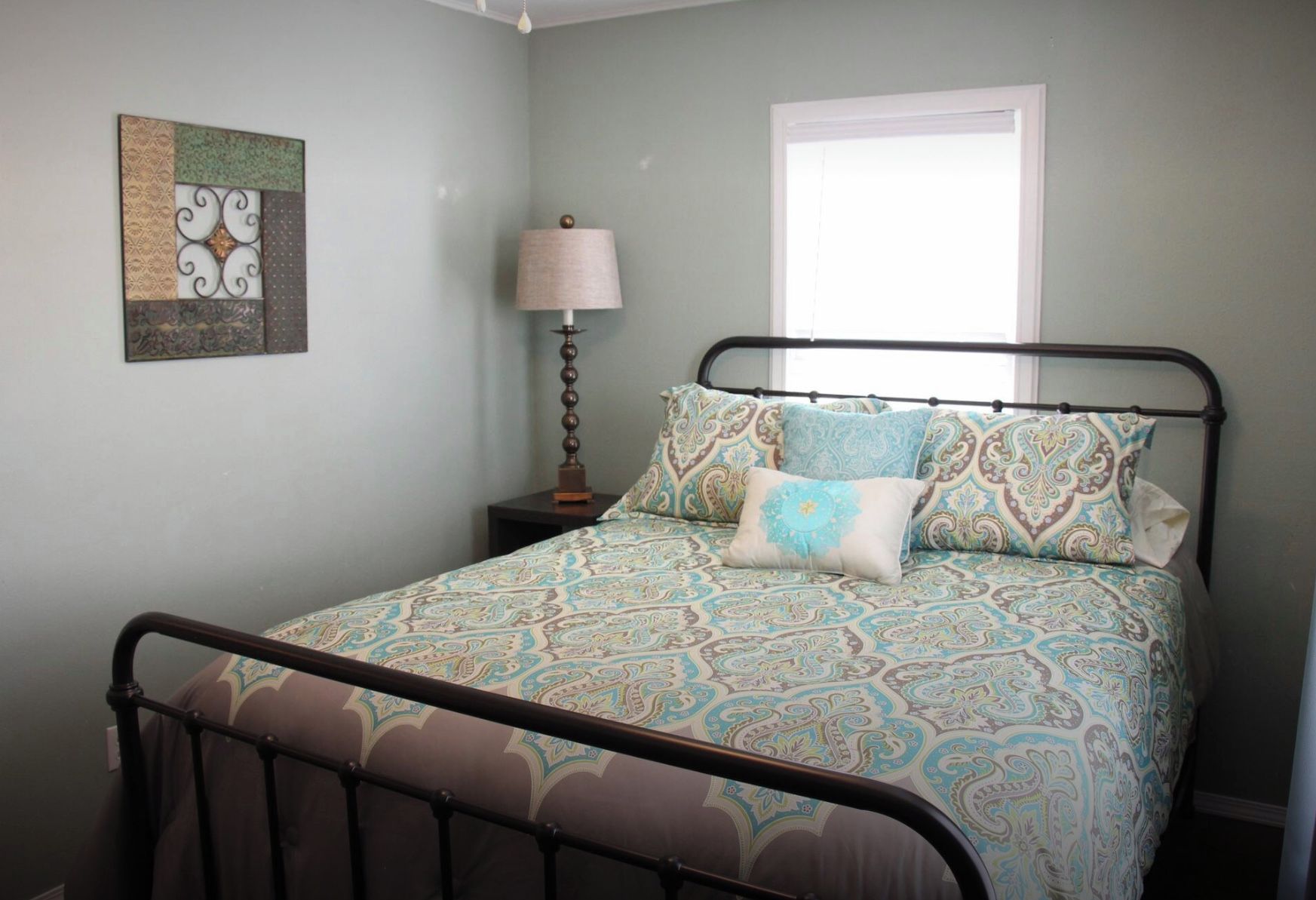 A bedroom with a bed, a nightstand, a lamp, and a window.