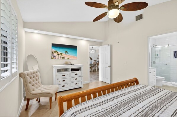 A bedroom with a bed, a chair, a dresser, a ceiling fan, and a bathroom with a shower.