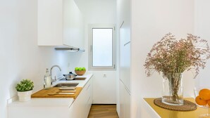 A narrow kitchen with white cabinets, a wooden countertop, a sink, and a window above the door.