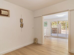 A spacious room with a wooden floor, a white chair, and a sliding glass door leading to an outdoor area.