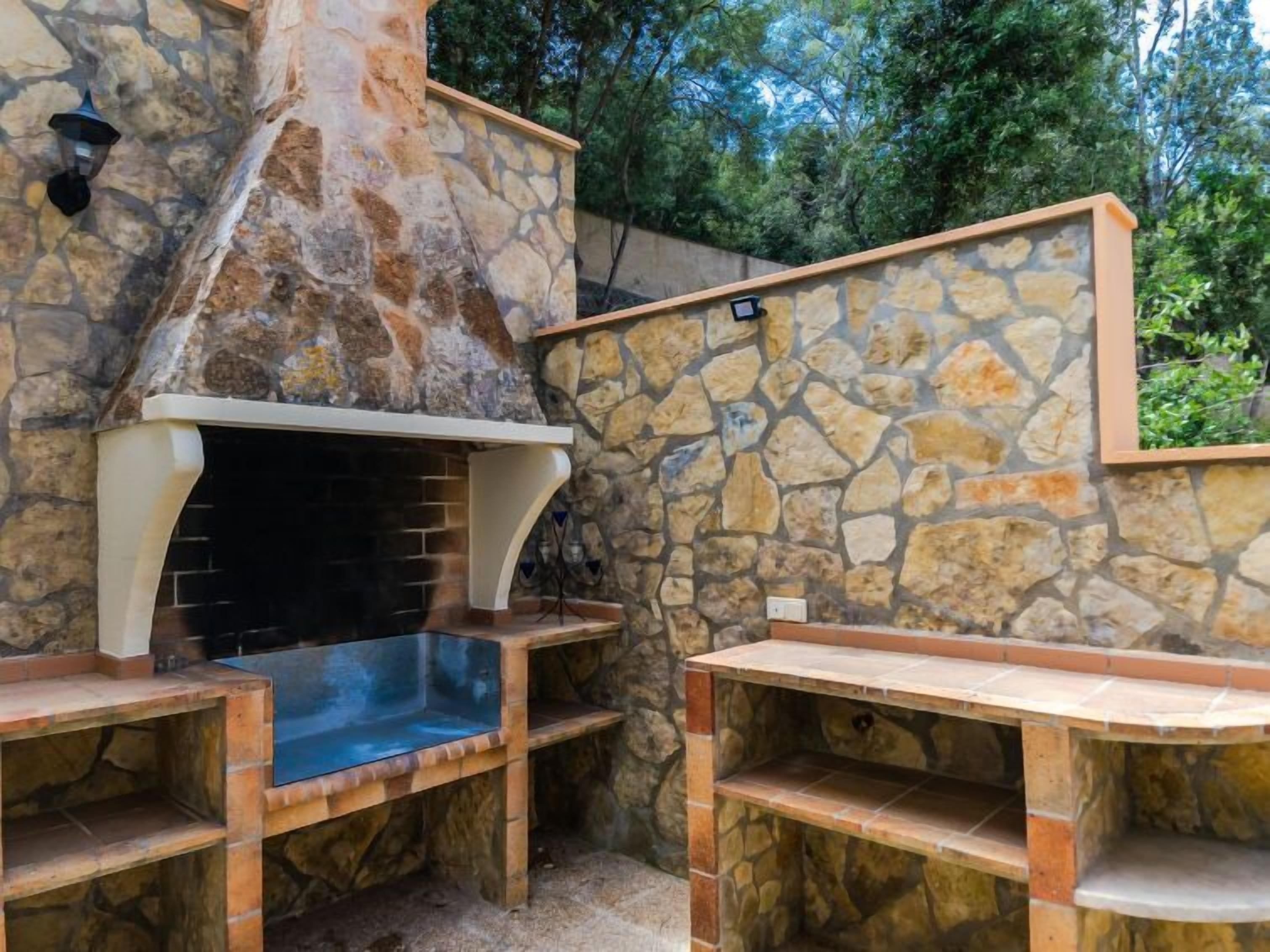 Un área de barbacoa de piedra al aire libre con chimenea, estantes empotrados y un muro de piedra.