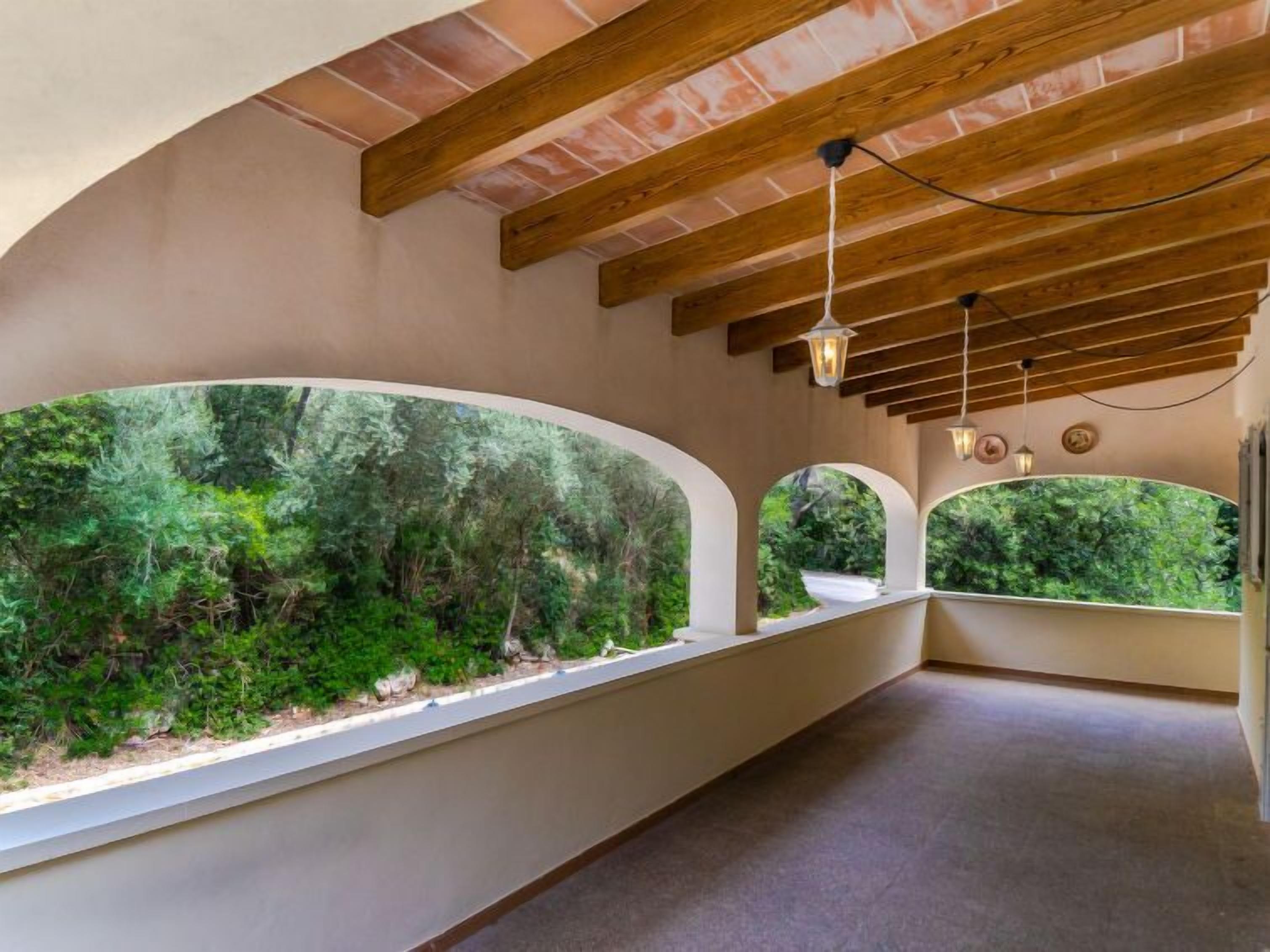 Una habitación con amplios ventanales de arco que dan a un exuberante jardín, vigas de madera en el techo y un diseño sencillo y limpio.