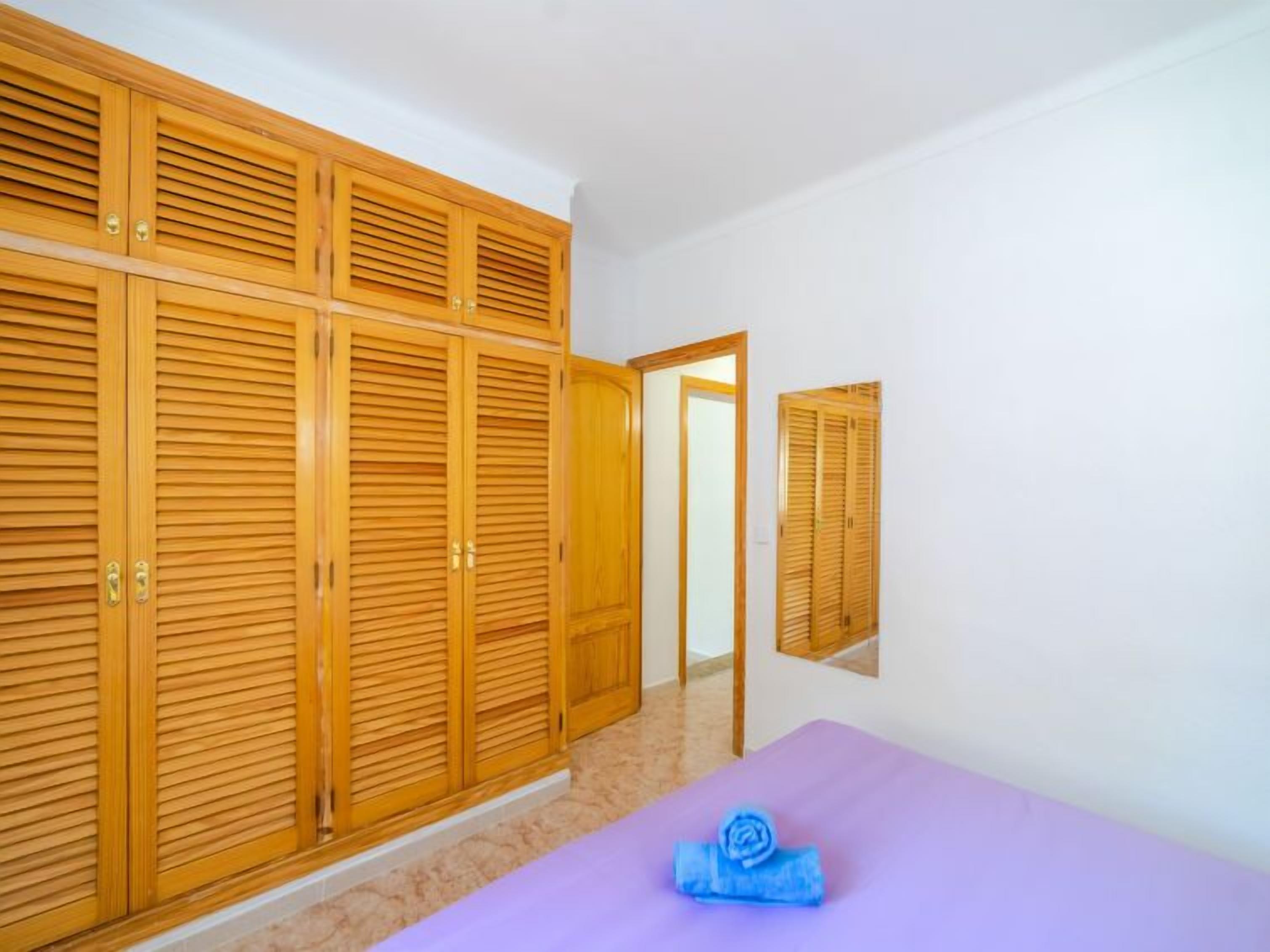 Een slaapkamer met een grote kast, een bed met een paars dekbed en een spiegel aan de muur.