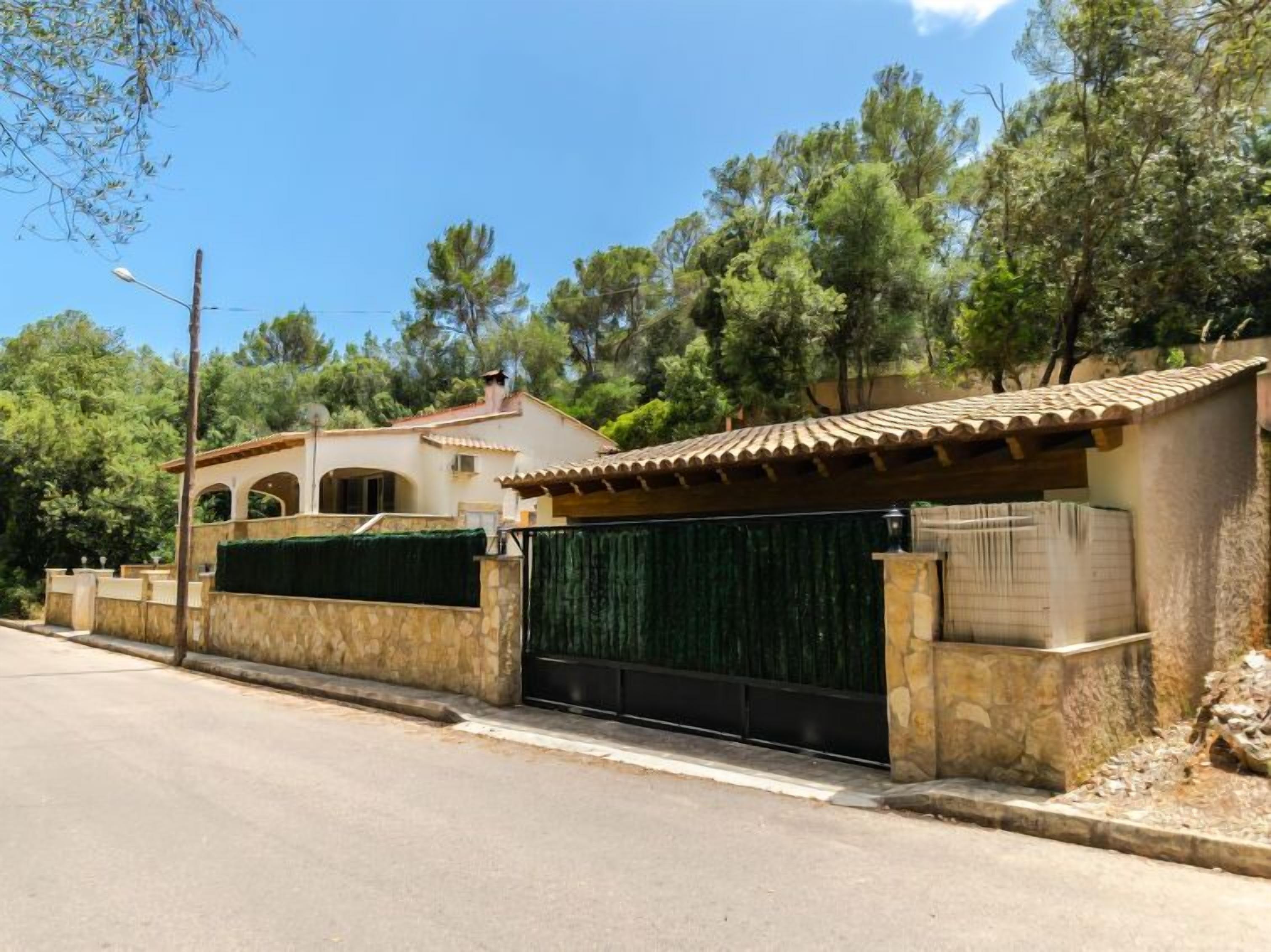 A villa with a tiled roof, a stone wall, and a gated entrance.