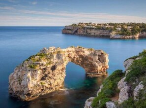A natural rock arch formation surrounded by calm sea and a coastal village. - Cala Santanyí Beach House JM by Interhome (Cala Santanyí-Figuera-Llombards)