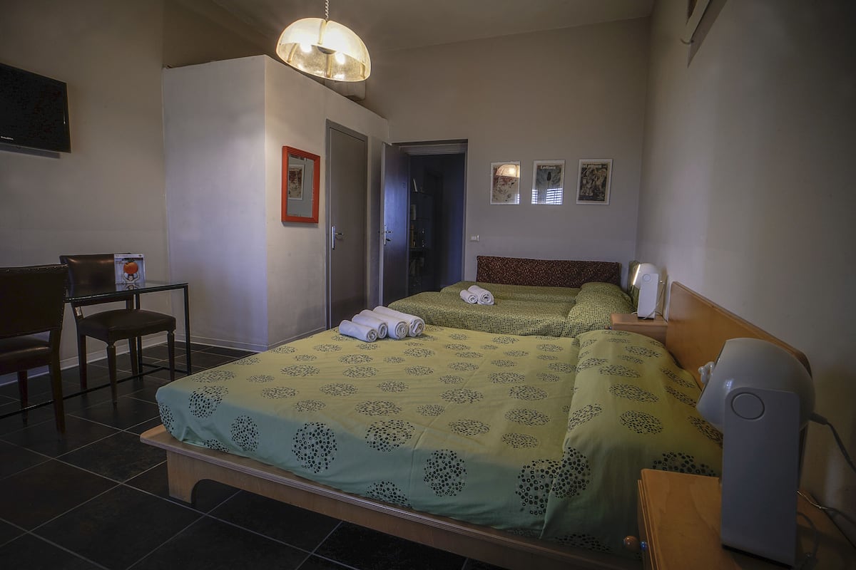 A hotel room with a bed, a desk, a chair, and a bedside table with a lamp.