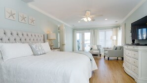 A spacious bedroom with a large bed, a ceiling fan, and a television.