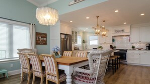 A spacious kitchen with white cabinetry, a dining area with wicker chairs, and a chandelier.