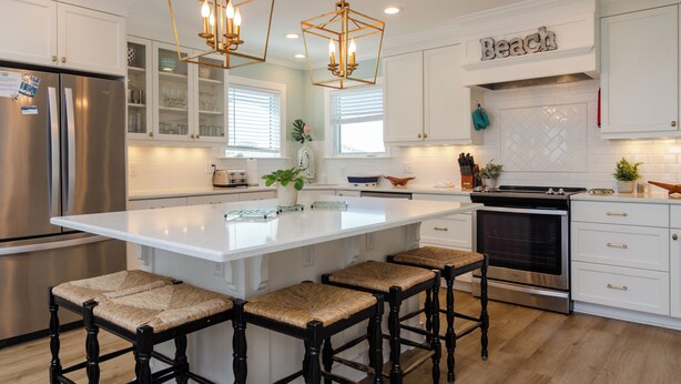 A modern kitchen with white cabinetry, a large island with bar stools, stainless steel appliances, and decorative lighting.