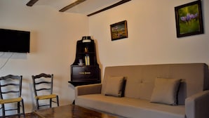 Un salon comprenant un canapé, deux fauteuils en bois, une table basse, un téléviseur fixé au mur et un piano.