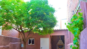 Une petite cour intérieure, fermée, avec un arbre, une porte et un mur en briques.