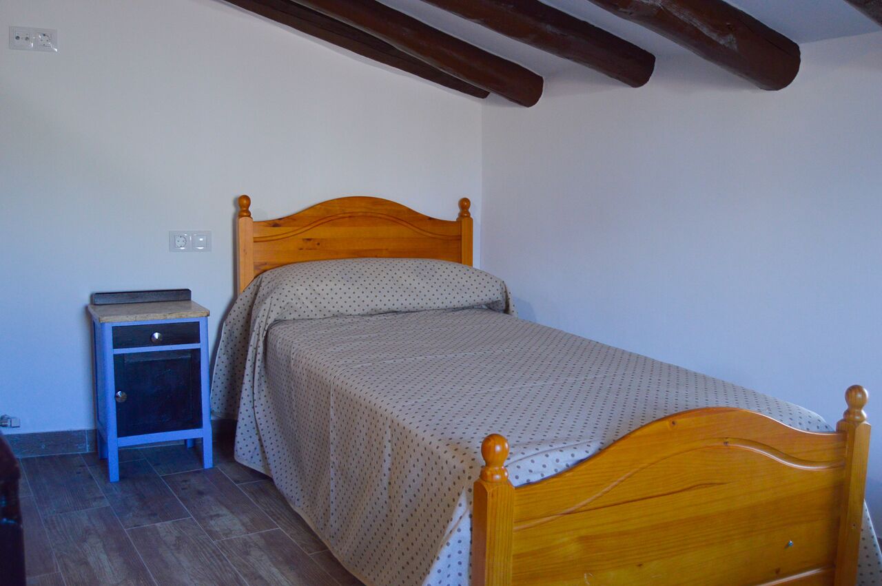 A single bed with a wooden headboard in a room with a small bedside table and a wall socket.