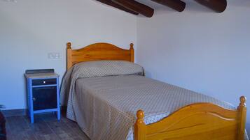 A single bed with a wooden headboard in a room with a small bedside table and a wall socket.
