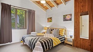 Ein Schlafzimmer mit Bett, Vorhängen, einem Fenster, einem Nachttisch, einer Lampe und einem Wandbild.