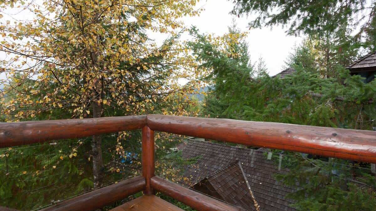 Holzgeländer einer Terrasse mit Blick auf einen Baum mit gelben Blättern und ein Gebäude mit geneigtem Dach.