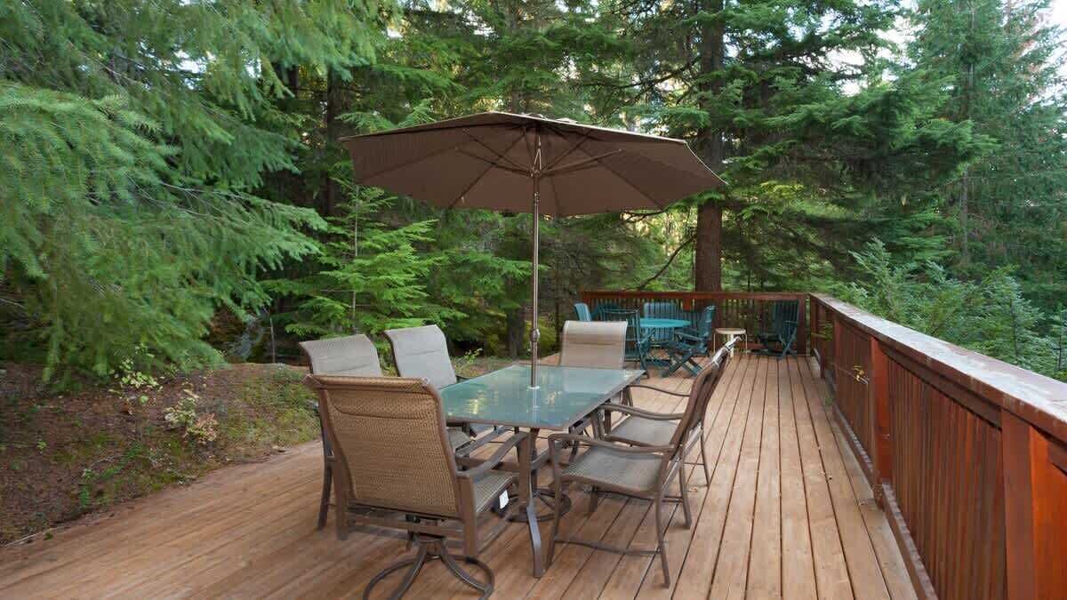 Eine Holzterrasse mit einem Glastisch und Stühlen, umgeben von dichtem Wald.
