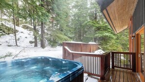 Un bain à remous sur une terrasse en bois, avec vue sur une forêt enneigée.