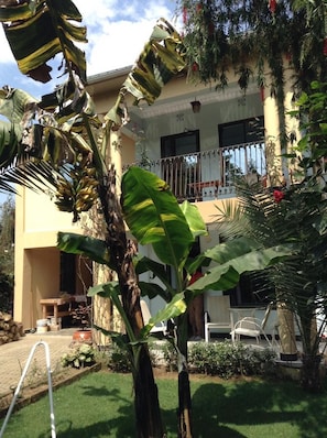 A two-story building with a balcony, surrounded by lush greenery and a well-maintained garden.