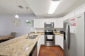 Une cuisine moderne avec des meubles blancs, des appareils en acier inoxydable, des plans de travail en granit et des luminaires suspendus.