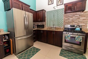 A kitchen with a stainless steel refrigerator, dark wooden cabinets, a microwave, a stove, and patterned backsplash tiles.