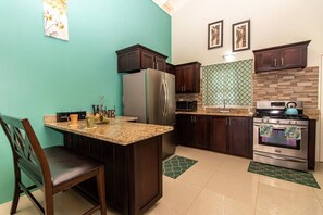 A kitchen with dark wooden cabinets, a stainless steel refrigerator, a microwave, a stove, and a green patterned backsplash.