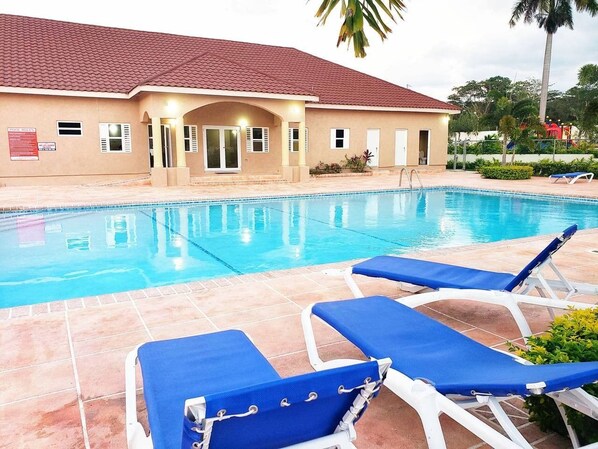 A swimming pool with blue lounge chairs and a building with a red-tiled roof.