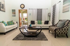 A living room with a sofa, armchair, coffee table, and a view of the outside.