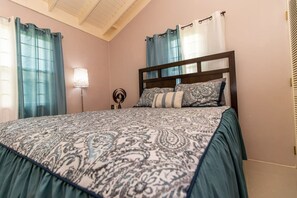 A bedroom with a bed, curtains, a bedside lamp, and a wall decoration.