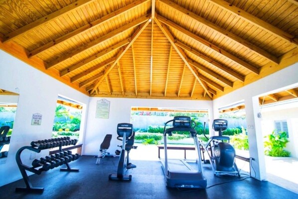 A covered gym with exercise equipment and a view of greenery.