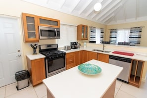 A modern kitchen with a stove, microwave, and dishwasher, wooden cabinets, and a large island with a decorative bowl.