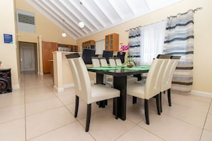 A dining area with a table and chairs, a ceiling with skylights, and a kitchen in the background.