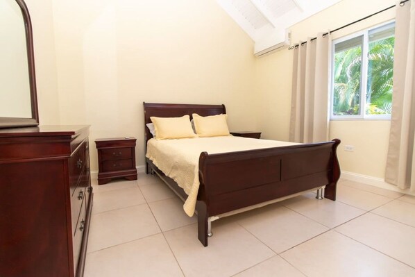 A bedroom with a bed, a nightstand, a dresser, and a window with curtains.