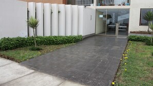 A modern building with a paved walkway, green plants, and a balcony with potted plants. - Departamento, 3 dormitorios, vista al Mar (San Miguel)