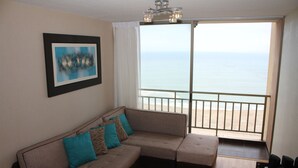A living room with a sofa, a round coffee table, and a view of the ocean through a balcony. - Departamento, 3 dormitorios, vista al Mar (San Miguel)