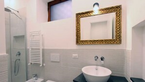 Un bagno moderno con cabina doccia in vetro, lavandino a colonna bianco e specchio con cornice dorata.